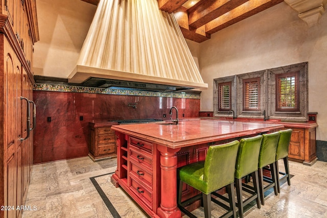 kitchen with a kitchen island with sink, a kitchen bar, premium range hood, and beam ceiling