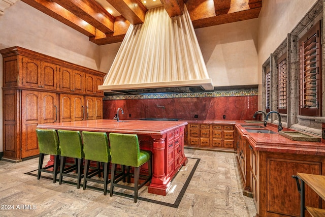 kitchen featuring a high ceiling, beamed ceiling, sink, a breakfast bar area, and an island with sink