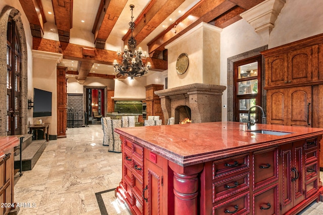 kitchen featuring a center island with sink, an inviting chandelier, hanging light fixtures, sink, and beamed ceiling