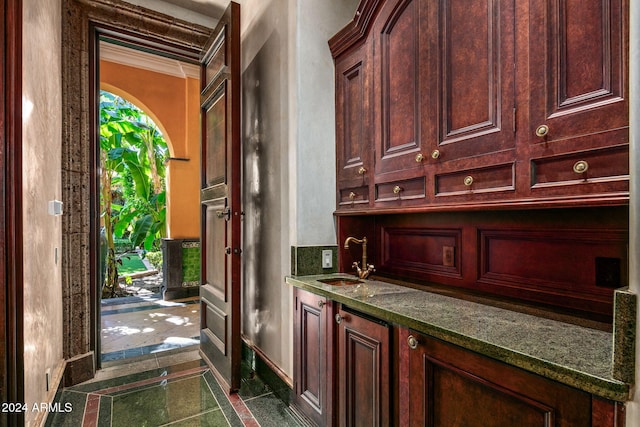 bar featuring ornamental molding, dark stone counters, and sink