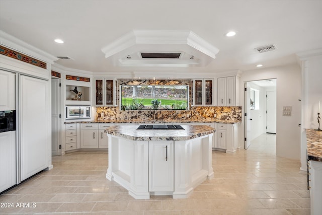 kitchen featuring white cabinets, a kitchen island, light stone countertops, and backsplash