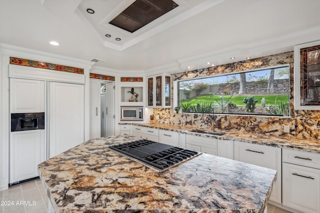 kitchen with backsplash, built in appliances, light stone counters, and white cabinets