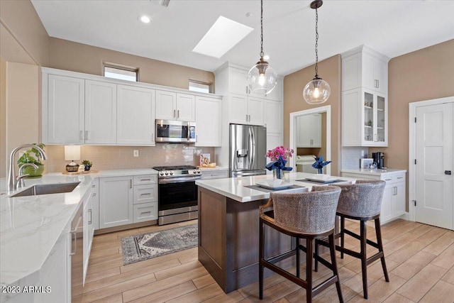 kitchen with appliances with stainless steel finishes, sink, a center island, light hardwood / wood-style floors, and white cabinets