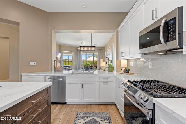 kitchen featuring appliances with stainless steel finishes, light hardwood / wood-style flooring, white cabinetry, and pendant lighting