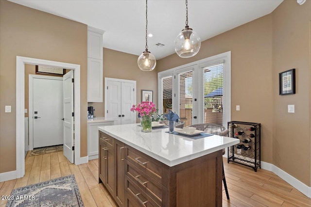 kitchen with a kitchen island, white cabinetry, light stone countertops, light wood-type flooring, and pendant lighting