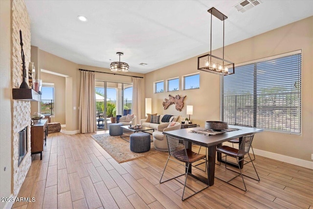 dining area with a stone fireplace, light hardwood / wood-style flooring, and an inviting chandelier