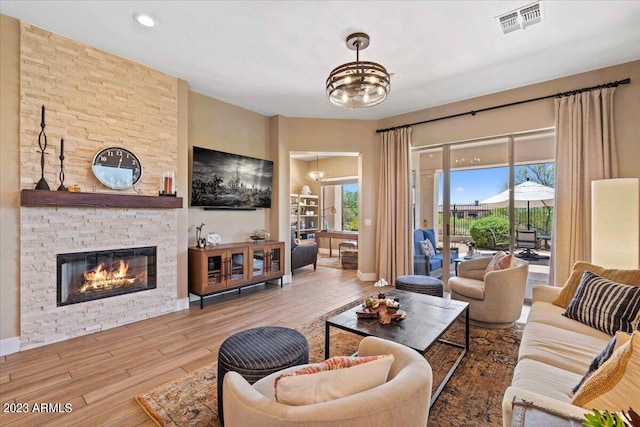 living room with a wealth of natural light, a notable chandelier, a stone fireplace, and wood-type flooring