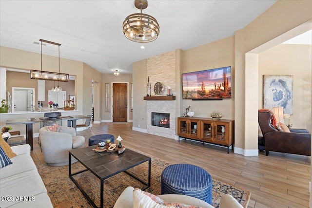 living room featuring a notable chandelier, light hardwood / wood-style floors, and a stone fireplace