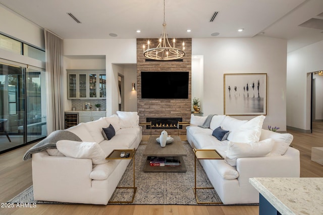 living area with a chandelier, wine cooler, wood finished floors, a brick fireplace, and recessed lighting