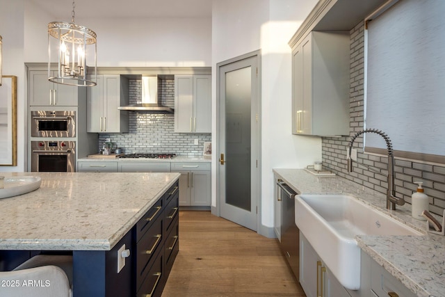 kitchen with wall chimney exhaust hood, a sink, appliances with stainless steel finishes, and tasteful backsplash