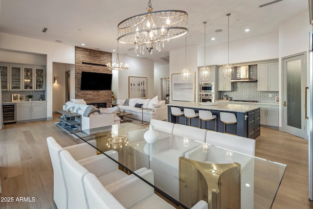 dining area with beverage cooler, a chandelier, light wood-style flooring, recessed lighting, and a fireplace