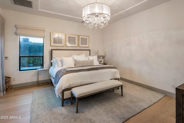 bedroom featuring light wood-type flooring, a chandelier, baseboards, and a tray ceiling