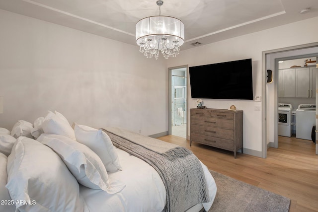 bedroom featuring washer and clothes dryer, a chandelier, light wood-style floors, baseboards, and a tray ceiling
