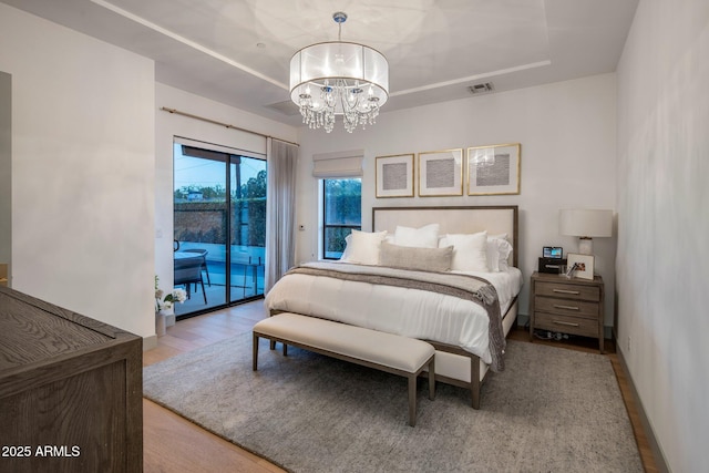bedroom with access to exterior, a chandelier, and wood finished floors