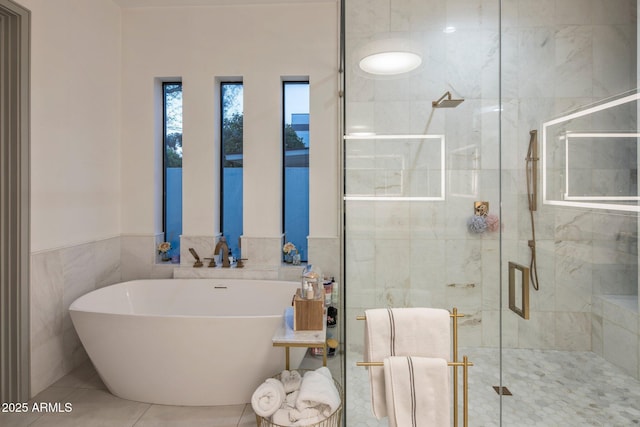 full bath featuring tile walls, a soaking tub, a stall shower, tile patterned flooring, and a wainscoted wall
