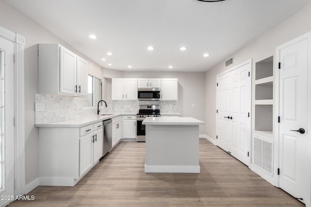 kitchen featuring appliances with stainless steel finishes, sink, white cabinets, a center island, and light wood-type flooring