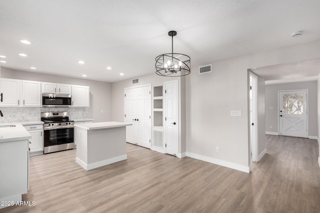 kitchen with stainless steel appliances, light wood-type flooring, hanging light fixtures, and white cabinets