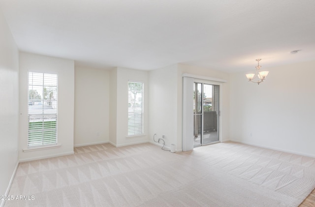 unfurnished room featuring a notable chandelier, baseboards, and light colored carpet