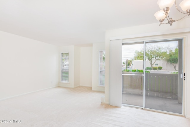 carpeted empty room with baseboards and an inviting chandelier