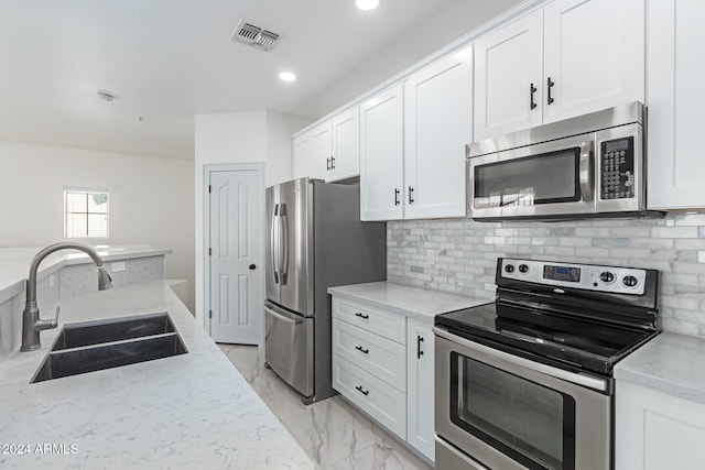 kitchen with appliances with stainless steel finishes, white cabinetry, light stone countertops, and sink