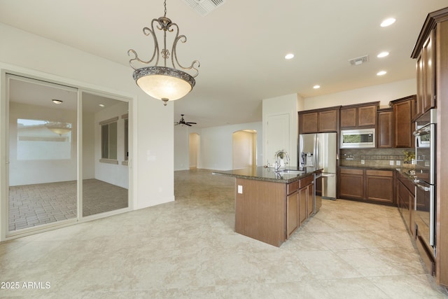 kitchen featuring sink, decorative light fixtures, stainless steel appliances, a kitchen island with sink, and backsplash