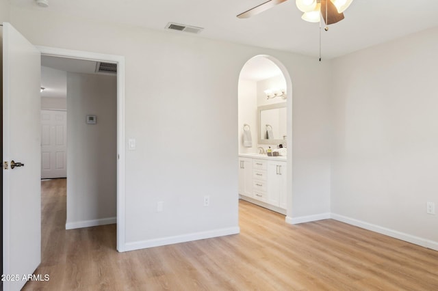 unfurnished bedroom featuring arched walkways, visible vents, baseboards, and light wood-style floors