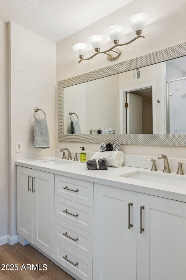 full bathroom featuring double vanity, visible vents, wood finished floors, and a sink