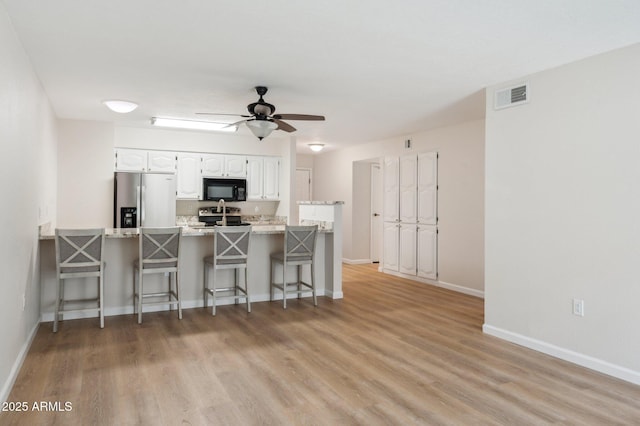 kitchen featuring visible vents, appliances with stainless steel finishes, a peninsula, a kitchen breakfast bar, and white cabinetry