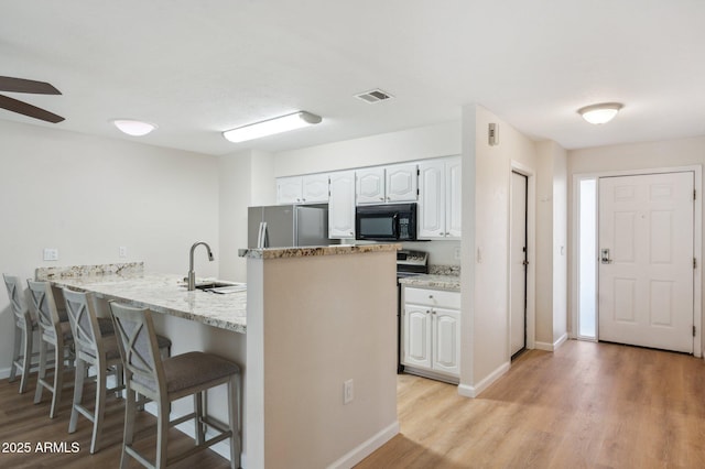 kitchen featuring visible vents, black microwave, a kitchen breakfast bar, freestanding refrigerator, and a sink