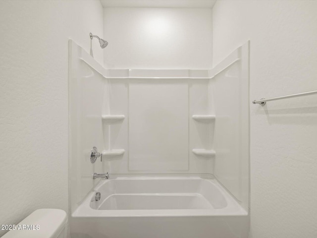 bathroom with a textured wall, shower / washtub combination, and toilet