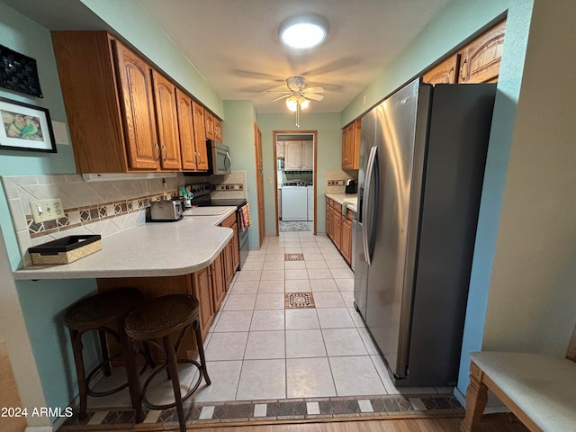 kitchen with appliances with stainless steel finishes, tasteful backsplash, ceiling fan, a breakfast bar area, and washer / clothes dryer