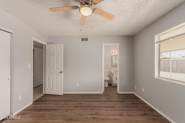 unfurnished bedroom featuring a textured ceiling, ceiling fan, dark wood-type flooring, and ensuite bathroom