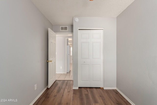 unfurnished bedroom with a textured ceiling, dark hardwood / wood-style floors, and a closet