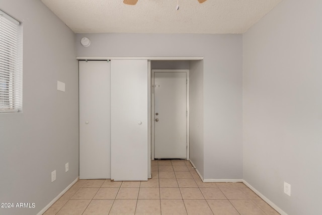 unfurnished bedroom featuring ceiling fan, light tile patterned flooring, a closet, and a textured ceiling