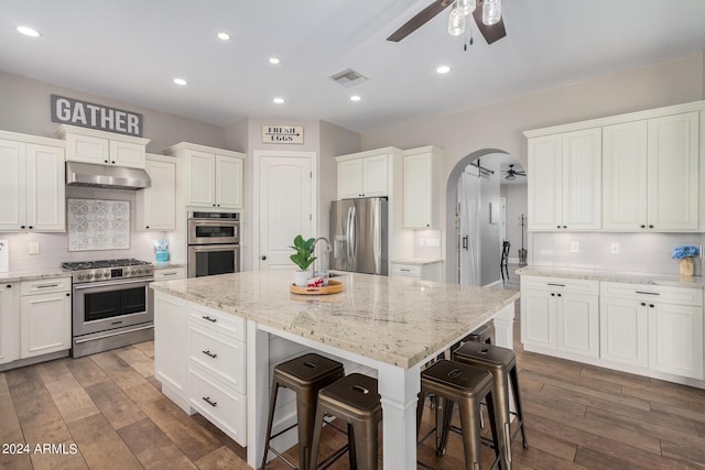 kitchen with visible vents, an island with sink, arched walkways, stainless steel appliances, and under cabinet range hood