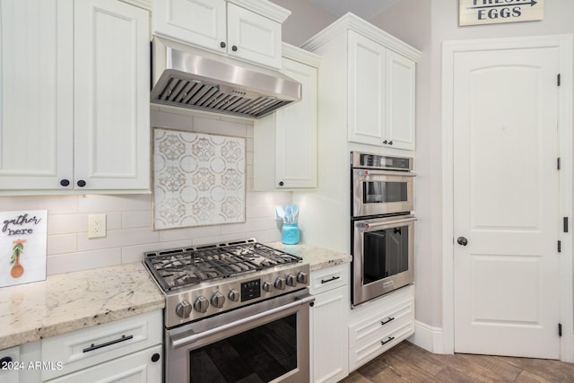 kitchen featuring under cabinet range hood, light stone counters, stainless steel appliances, white cabinets, and decorative backsplash