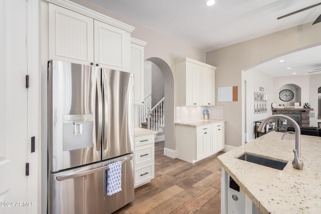 kitchen featuring light wood-style flooring, arched walkways, stainless steel fridge, a ceiling fan, and a sink