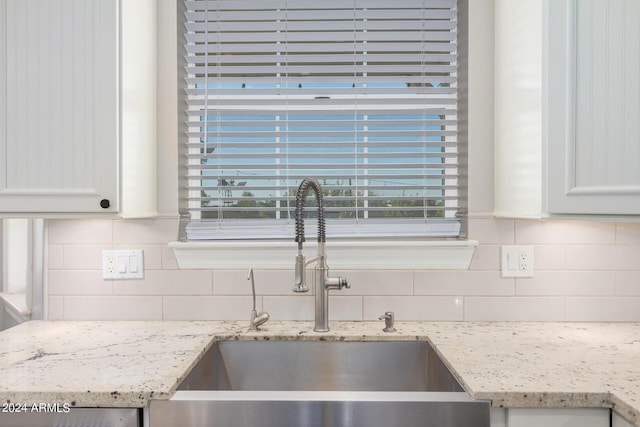 room details with backsplash, white cabinets, light stone countertops, and a sink