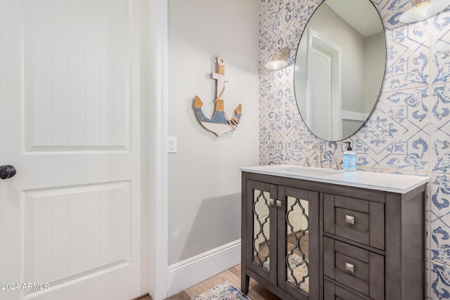 bathroom with baseboards, wood finished floors, vanity, and wallpapered walls