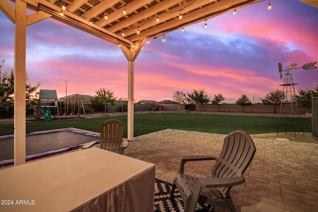 patio terrace at dusk with a lawn, a playground, and fence