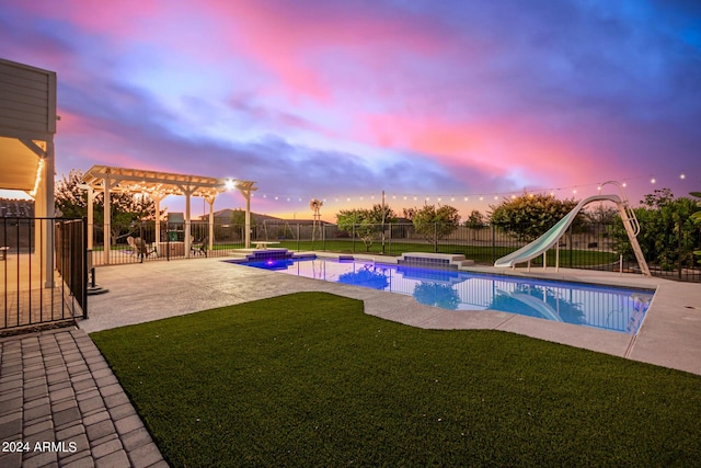 pool at dusk with a water slide, a fenced backyard, a yard, a pergola, and a patio