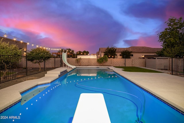 pool at dusk with a fenced in pool, a water slide, a fenced backyard, a diving board, and a patio area