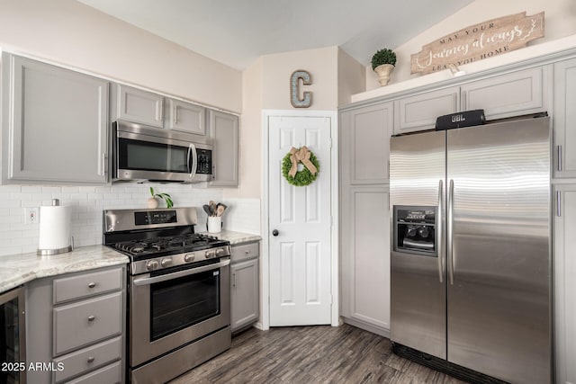 kitchen with stainless steel appliances, backsplash, gray cabinets, and light stone countertops