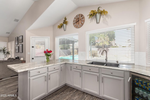 kitchen with beverage cooler, lofted ceiling, a peninsula, light stone countertops, and a sink