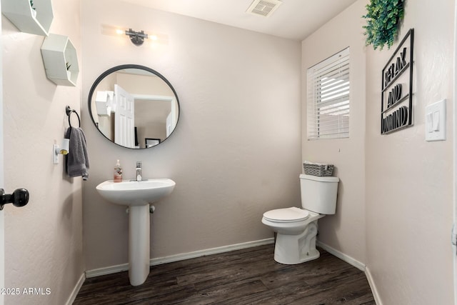 half bath with toilet, a sink, wood finished floors, visible vents, and baseboards