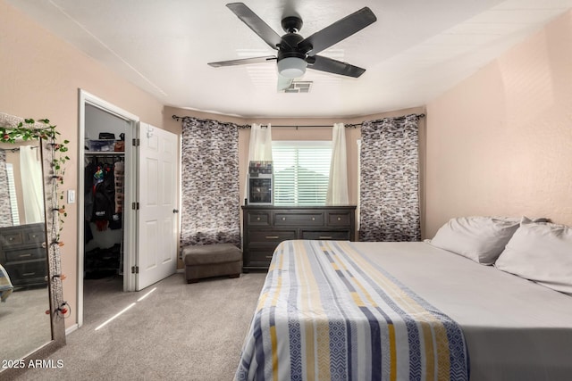 bedroom with light colored carpet, a ceiling fan, visible vents, a closet, and a walk in closet