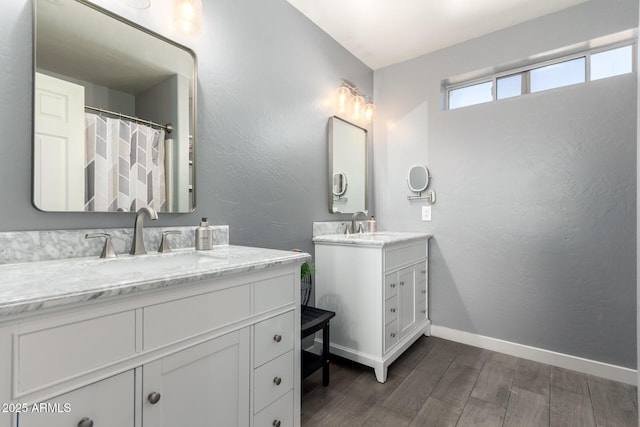 bathroom with two vanities, a textured wall, a sink, wood finished floors, and baseboards