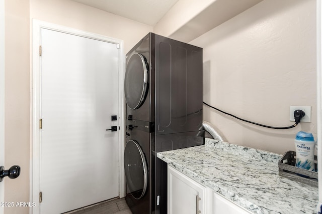 laundry room featuring stacked washing maching and dryer, light wood finished floors, and cabinet space