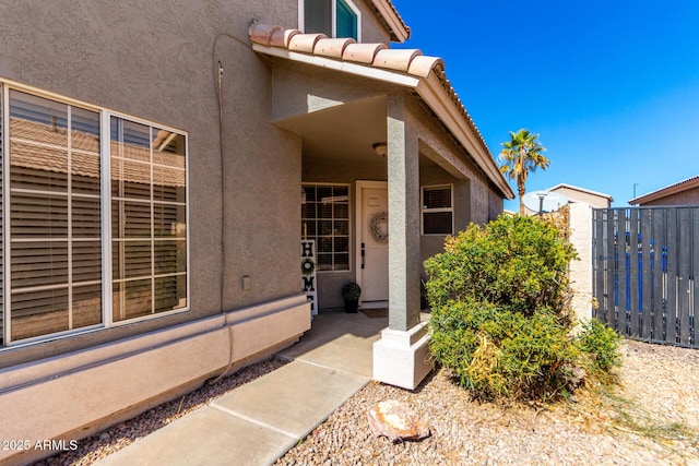 entrance to property featuring a tile roof, fence, and stucco siding