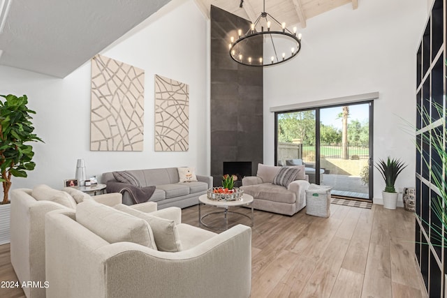 living room with high vaulted ceiling, an inviting chandelier, light hardwood / wood-style flooring, beamed ceiling, and a tiled fireplace